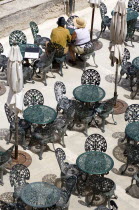 Couple of people sitting at a table amongst other wrought iron tables and chairs in a cafe below the Upper Barrakka Gardens overlooking Valletta Harbour