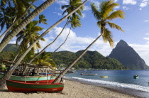 Fishing boats on the beach lined with coconut palm trees with the town and the volcanic plug mountain of Petit Piton beyond