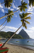 Fishing boats on the beach lined with coconut palm trees with the town and the volcanic plug mountain of Petit Piton beyond