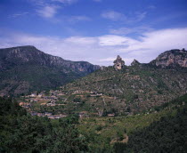 View across Gorge de la Jonte junction with the Tarn Gorge at Le Rozier village set on terraced hillside topped with pinnacles of eroded rock.