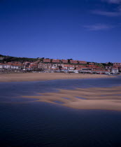 Town buildings extending to sea wall with moored boats on sand bars at low tide on the Rio del Escudo estuary.