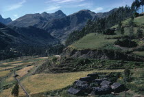 Settlement of houses with thatched roofs surrounded by green hills and slopes with sheep grazing on grass ridges and mountains behindAmerican Bolivian Farming Agraian Agricultural Growing Husbandry...