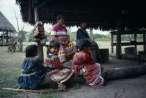 Independent Seminole Native American village. Family of women and young girls wearing traditional colourful patchwork dresses sitting under a Chickee hut.North America United States of America Americ...