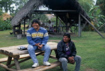 Independent Seminole Native American village. Two men named Danny and Billie sitting on a wooden bench smiling with a Chickee hut behindNorth America United States of America American 2 Happy Male Ma...