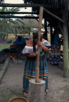 Independent Seminole Native American village. Woman pounding corn wearing traditional colourful patchwork clothing Classic Classical Colorful Farming Agraian Agricultural Growing Husbandry  Land Prod...