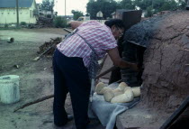 Zuni Pueblo Native American Indian woman making bread in a Horno mud adobe outdoor oven American North America United States of America Female Women Girl Lady Hispanic Latin America Latino Mexican On...