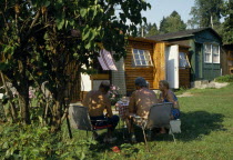 Cernosice Holiday Homes. Elderly couples sitting around a table on the grass outside wooden chalets.Ceska Eastern Europe European Old Senior Aged