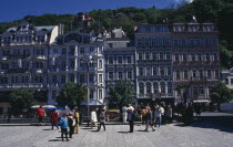 Square in spa city with crowds of visitors overlooked by tall  narrow buildings painted in pastel colours. Ceska Eastern Europe European