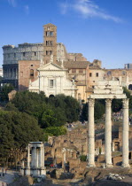 View of the Forum with the Colosseum rising behind the bell tower of the church of Santa Francesca Romana with tourists walking past the Temple of Vesta and the three Corinthian columns of the Temple...