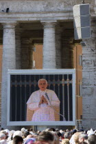 Vatican City Pilgrims in St Peters Square for the wednesday Papal Audience in front of the Basilica watching Pope Benedict XVI Joseph Alois Radzinger with a cardinal on a large video TV monitor displa...