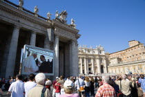 Vatican City Pilgrims in St Peters Square for the wednesday Papal Audience in front of the Basilica watching Pope Benedict XVI Joseph Alois Radzinger with a cardinal on a large video TV monitor displa...