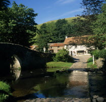 Malmsmead on Badgworthy Water. Arched stone bridge and ford across river leading to  Lorna Doone Farm  shop White painted building with tiled roof  and outbuildings.rural countyside village vernacula...