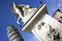 The Campo dei Miracoli or Field of Miracles.The Leaning Tower or Torre Pendente belltower with tourists on the top level under a blue sky with a statue and water fountain with cherubs in the foregroun...