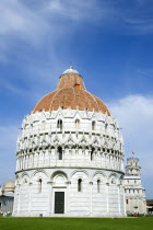 The Campo dei Miracoli or Field of Miracles.The Baptsitry with tourists on the grass with the Leaning Tower or Torre Pendente beyond under a blue skyEuropean Italia Italian Southern Europe Toscana Tu...