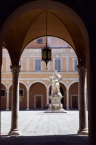 Courtyard statue and pink buildings seen through an archway with columnsEuropean Italia Italian Southern Europe Toscana Tuscan