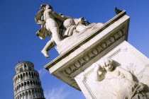 Campo dei Miracoli or Field of Miracles Statue of cherubs with a carving of a cherub and bearded mans face on a water fountain in front of the Leaning Tower belltower or Torre Pendente under a blue sk...