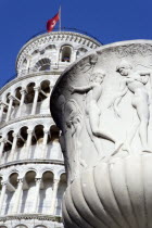 Campo dei Miracoli or Field of Miracles Urn or vase with carving of naked classical male characters in front of the Leaning Tower belltower or Torre Pendente under a blue skyEuropean Italia Italian S...