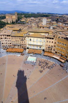 Shadow of the Torre del Mangia campanile belltower in the Piazza del Campo with surrounding buildings and rooftops and the countryside beyond.The square busy with touristsEuropean Italia Italian Sout...