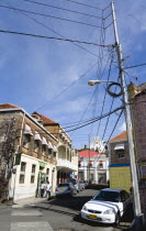 People walking down a side street lined with parked cars in the capital with overhead electricity power and telephone cables.Caribbean Destination Destinations Grenadian Greneda West Indies Grenada A...