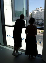 Young silhouetted couple looking out the window of the Towner Gallery building toward the seafront.European Great Britain Northern Europe UK United Kingdom British Isles Holidaymakers Immature Touris...