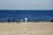 Man and young boy on the beach with deck chairs blowing in the wind. Speed passing by in the distance.European Great Britain Northern Europe UK United Kingdom British Isles Beaches Holidaymakers Imma...