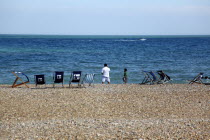 Man and young boy on the beach with deck chairs blowing in the wind. Speed passing by in the distance.European Great Britain Northern Europe UK United Kingdom British Isles Beaches Holidaymakers Imma...