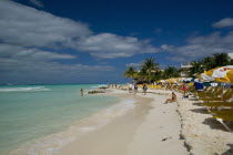 Isla Mujeres exotic tropical beach with blue-sky and white clouds and one person ready to swim at the crystal clear seawater while others are walking and sunbathing at the coastline or relaxing at the...