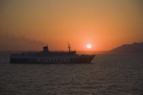 Sun sets behind Greek Ferry with coast of Nisyros to right  on ferry route between Rhodes and Kos.Greek islandsDodecaneseRhodesRhodosRodiAegeanMediterraneanEuroholidayUNESCOCruiseportharb...