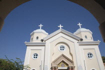 Agia Paraskevi Church.  White and cream exterior facade against blue sky framed by silhouetted archway. Greek islandsDodecaneseKosHippocratesHippocraticAegeanMediterraneanEuroholidayCruisep...