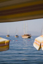 View across bay towards gulf of Gokova from beneath sun parasols part framing flat  calm water with yachts and Gulet boats. Turkish Aegean coastmediterraneanresortformerly HalicarnassusHalikarnas...