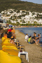 Line of brightly coloured bean-bags set out along beach for late afternoon cafe and restaurant trade.  White painted buildings spread across hillside beyond.Turkish Aegean coastmediterraneanresort...