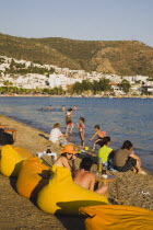 Line of brightly coloured bean-bags set out along beach for late afternoon cafe and restaurant trade.  White painted buildings spread across hillside beyond.Turkish Aegean coastmediterraneanresort...