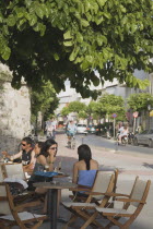 People drinking at tables beneath tree outside cafe.Greek IslandsResort Summer Clear Blue Sky early season Aegean DodecaneseDestination Destinations Ellada European Greek Southern Europe Bar Bistro...