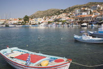 Red  blue and white painted rowing boat moored in the habour with town on hillside beyond.Greek IslandsResort Summer Clear Blue Sky early season Aegean Dodecanese Destination Destinations Ellada Eur...