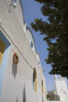 Agia Paraskevi Greek Orthodox Church.  Angled view of white exterior facade with pale blue and yellow painted window recesses.Greek IslandsAegeanMediterraneanKossummerseasonholidayDestination...