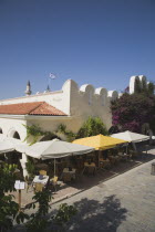 Plateia Eleftherias town square showing cafe at entrance to market with outside tables situated in shade of sun umbrellas.Greek IslandsAegeanMediterraneanKossummerseasonholidayDestination Dest...