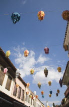 Strings of coloured lanterns hanging between buildings against blue sky with white cloud.TurkishAegeancoastresortsummersunshineearly summer seasonMediterraneanholidayDestination Destinations...