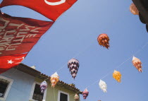 Coloured lanterns and Turkish flag hanging between part seen buildings against clear blue sky.TurkishAegeancoastresortsummersunshineearly summer seasonMediterraneanholidayDestination Destina...