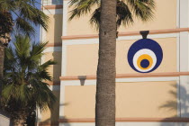 Circular  painted blue  white and yellow design on cream coloured wall with palm trees in foreground. TurkishAegeancoastresortsummersunshineearly summer seasonMediterraneanholidayDestination...