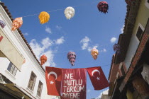 Turkish flag and coloured lanterns hanging between partly seen buildings.TurkishAegeancoastresortsummersunshineearly summer seasonMediterraneanholidayDestination Destinations Ellada European...