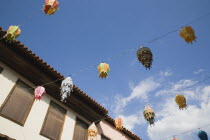 Coloured lanterns hanging between partly seen buildings against blue sky with white clouds.TurkishAegeancoastresortsummersunshineearly summer seasonMediterraneanholidayDestination Destinatio...