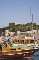 Cruise boats moored in harbour with fortified building on tree covered hilltop beyond.TurkishAegeancoastresortSummersunshineearly Summer seasonholidaydestinationdestinations ElladaEuropean...