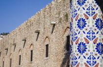 Detail of pillar decorated with painted tiles in blue  red and green stylised floral motif with fortified stone wall behind.TurkishAegeancoastresortSummersunshineearly Summer seasonholidaydes...