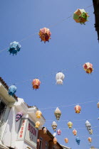 Lines of coloured lanterns hanging across street from part seen buildings against clear blue sky.TurkishAegeancoastresortSummersunshineearly Summer seasonholidaydestinationDestinations Ellad...