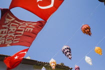 Lines of coloured lanterns and Turkish flags hanging across street from part seen buildings against clear blue sky.TurkishAegeancoastresortSummersunshineearly Summer seasonholidaydestination...