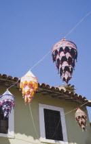 Lines of coloured lanterns hanging across street from part seen pastel and white painted building against clear blue sky.TurkishAegeancoastresortSummersunshineearly Summer seasonholidaydestin...