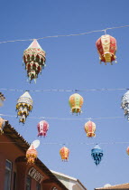 Lines of coloured lanterns hanging across street from part seen buildings against clear blue sky.TurkishAegeancoastresortSummersunshineearly Summer seasonholidaydestinationdestinations Ellad...