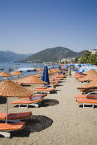 Line of sun loungers and parasols for rent along beach in morning sun overlooking sea  apartments and headland beyond.resortholidayholidaymakersDestinationCrowdedcrowdsun umbrellashadesun lou...