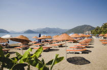 Marmaris on the Turkish Riviera in early Summer season.  Parasols and sunbeds for rent on the beach in morning sun. coastcoastalholidaymakerssunviewblue skyclearsearelaxingleisuresunbathing...