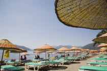 Marmaris on the Turkish Riviera in early Summer season.  Lines of parasols and sunbeds for rent on the beach in morning sun. coastcoastalresortholidayholidaymakerssunrelaxingleisuresuntansun...